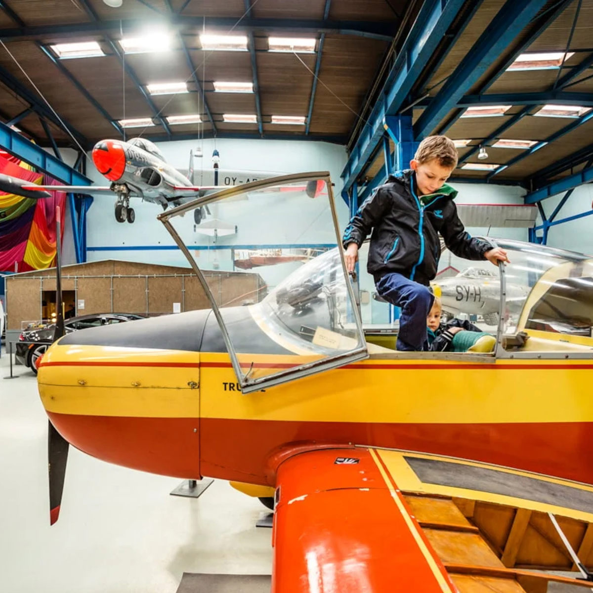 Barn klättrar in i gul och röd flygmaskinmodell Fly i flygmuseum.