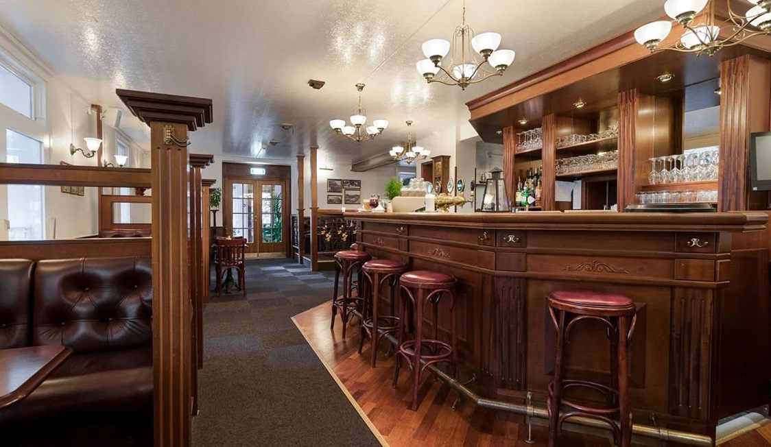 Gilleleje Strand Hotel Pub med klassisk träinredning, eleganta barstolar och upplyst interiör.
