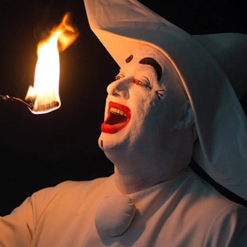 Mande i hvid maske og hat optræder med ildspisning i en dramatisk forestilling.