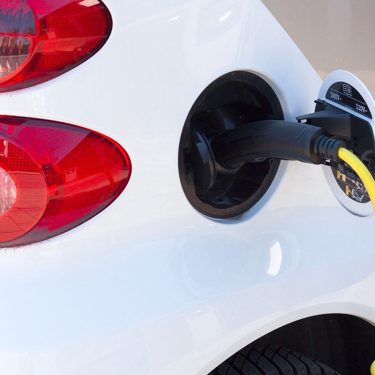White electric car charging with a black and yellow cable close-up near the taillight.