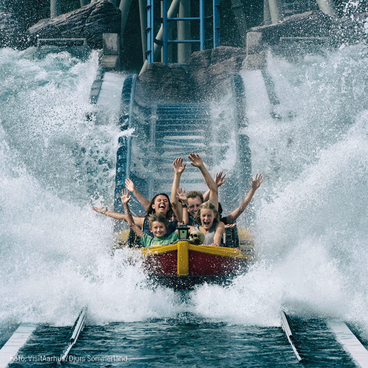 Familie nyder vildt vandrutsjebane-eventyr i Djurs Sommerland med hænderne i vejret og smil på ansigterne.
