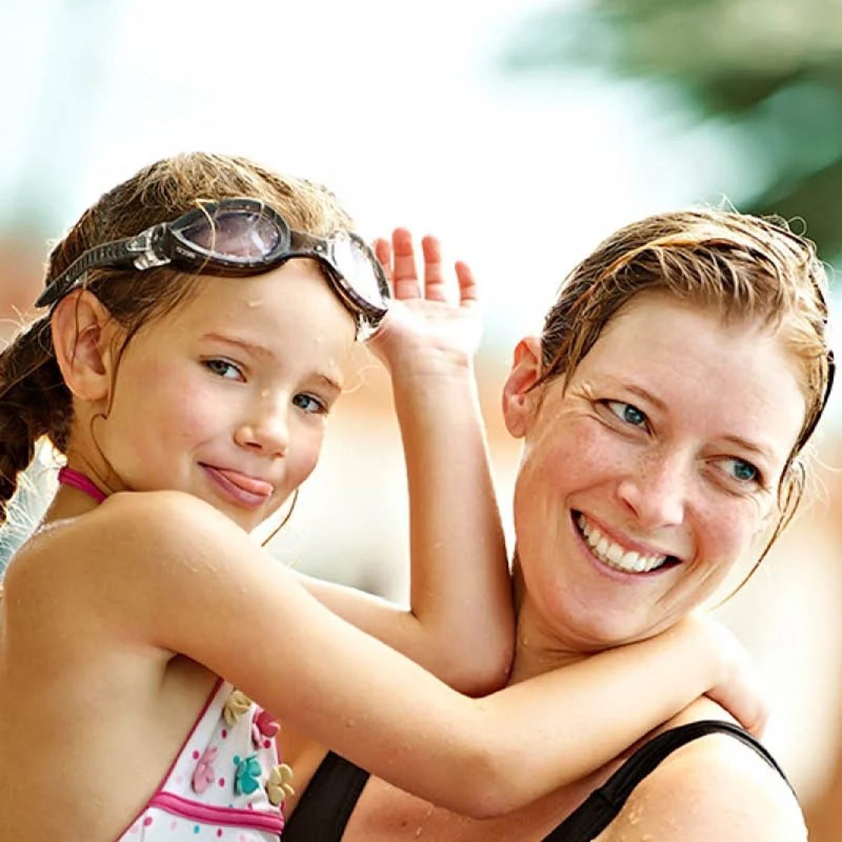 Mor och dotter skrattar tillsammans på vattenpark, dottern bär simglasögon på huvudet.