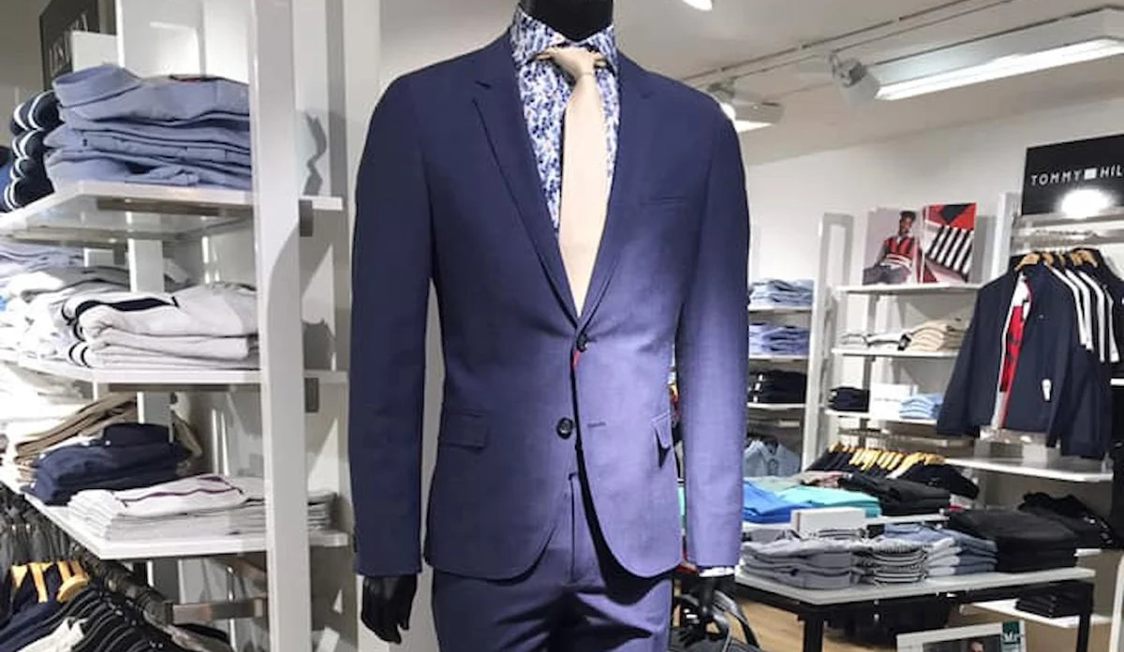 Mraugust kostym i blått på skyltdocka med mönstrad skjorta och beige slips i klädbutik.