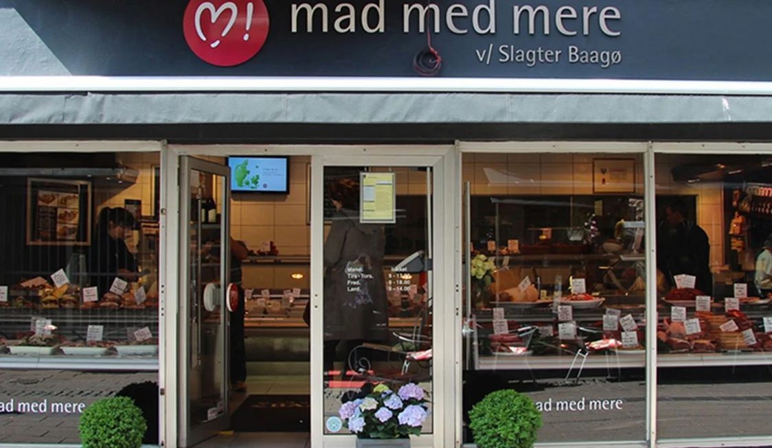 Slagteri Helsingörs affärsfasad med köttprodukter i skyltfönstret och Blomsterdekorationer framför ingången.