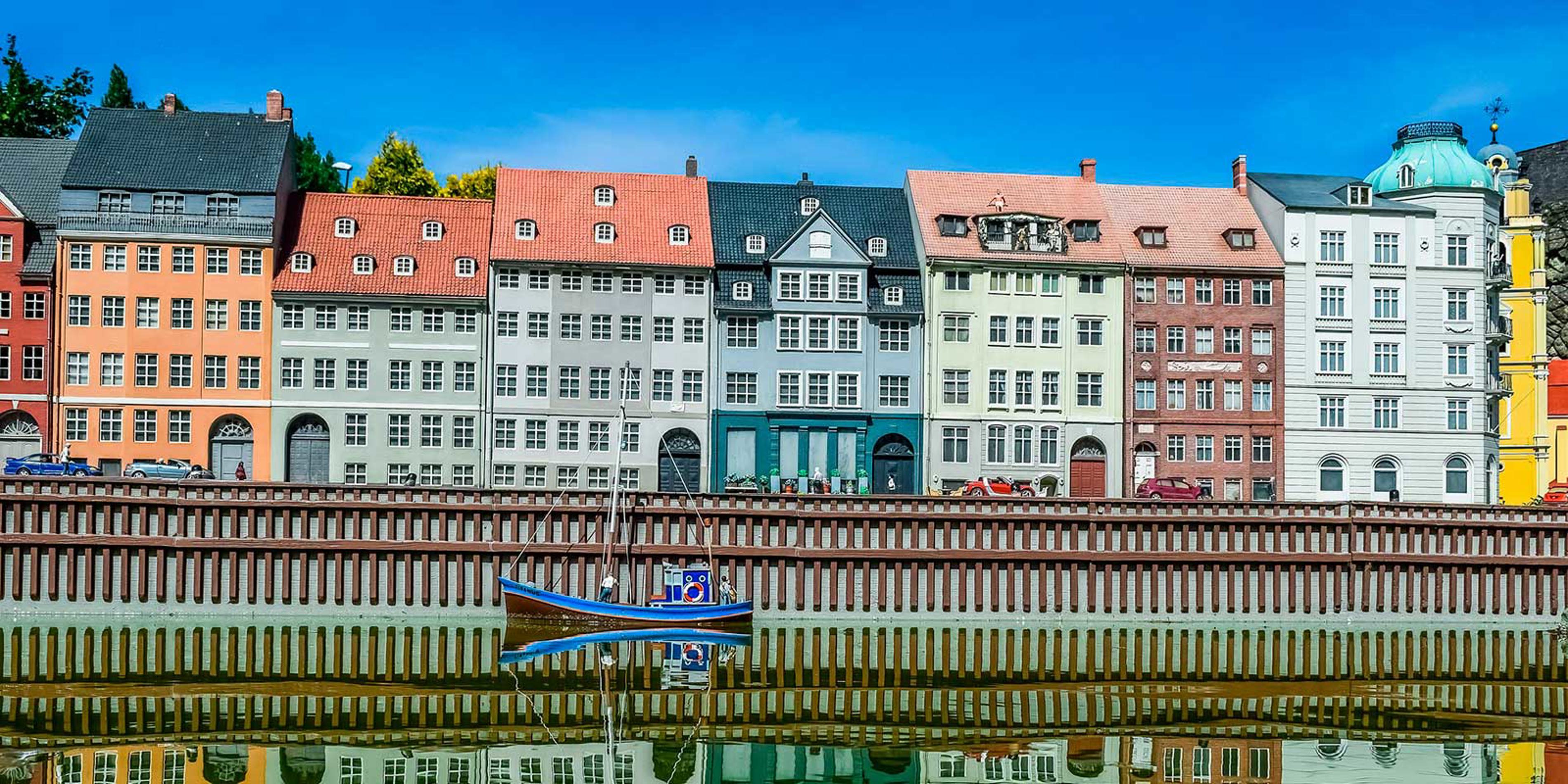Färgglada husfasader i Köpenhamn längs en kanal med en blå båt i förgrunden, speglade i vattnet.