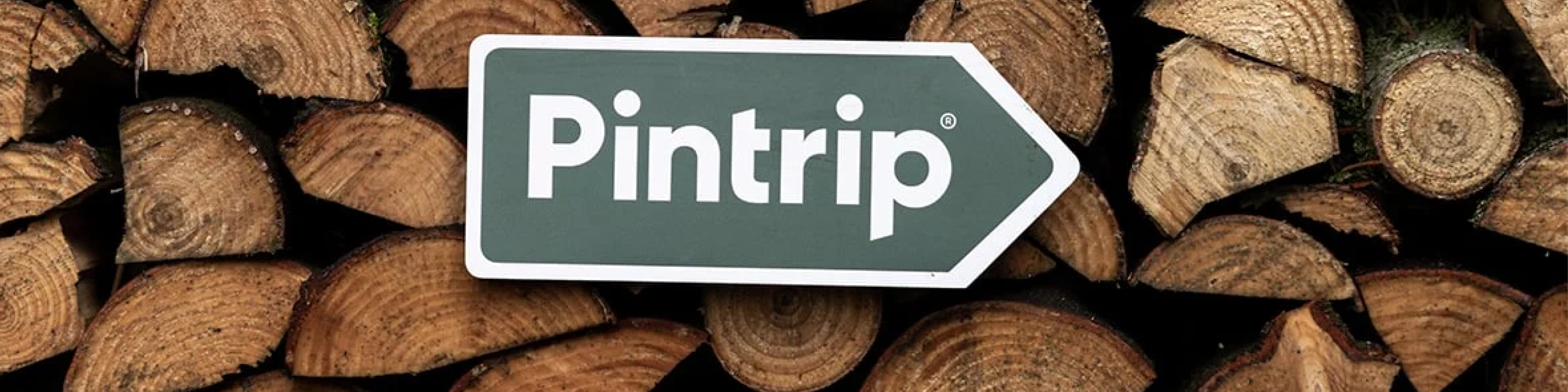 Pintrip skilt i en skov af stablet skovtræ med grøn baggrund og hvid tekst.