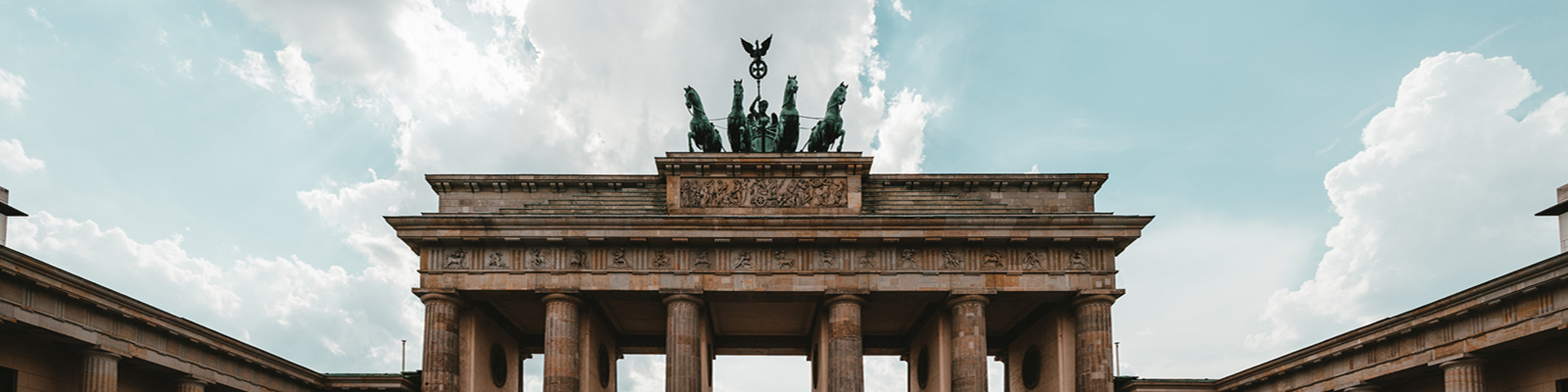 Brandenburger Tor i Berlin mot molnig himmel, sedd framifrån med skulpturer och arkitektoniska detaljer tydligt synliga.