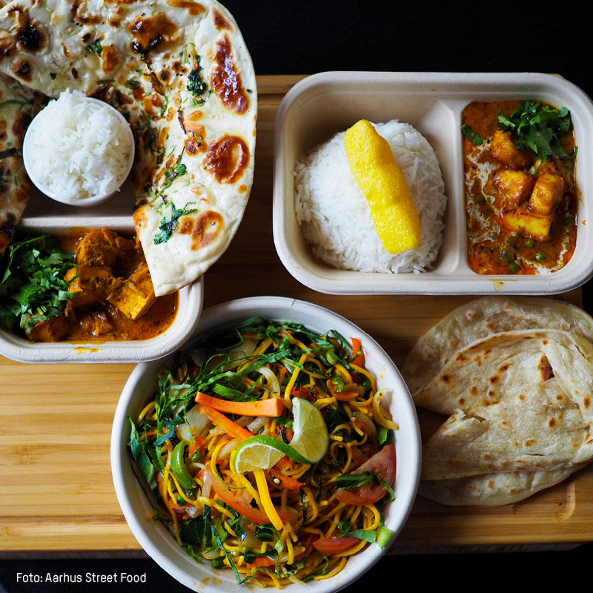 Indisk gadekøkkenmåltid med farverig salat, karry med ris, naanbrød og chapati serveret på træbræt.