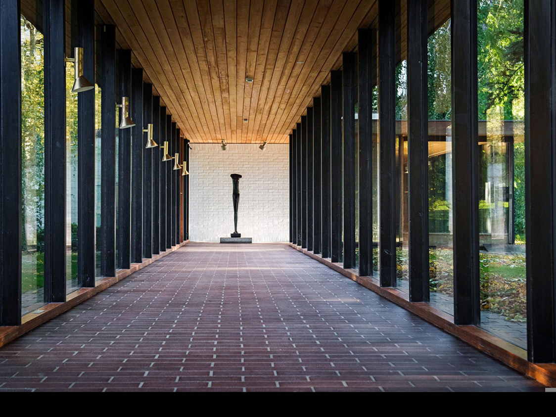 Konstskulptur i slutet av en glasgång med tegelgolv och trätak på Louisiana Museum.