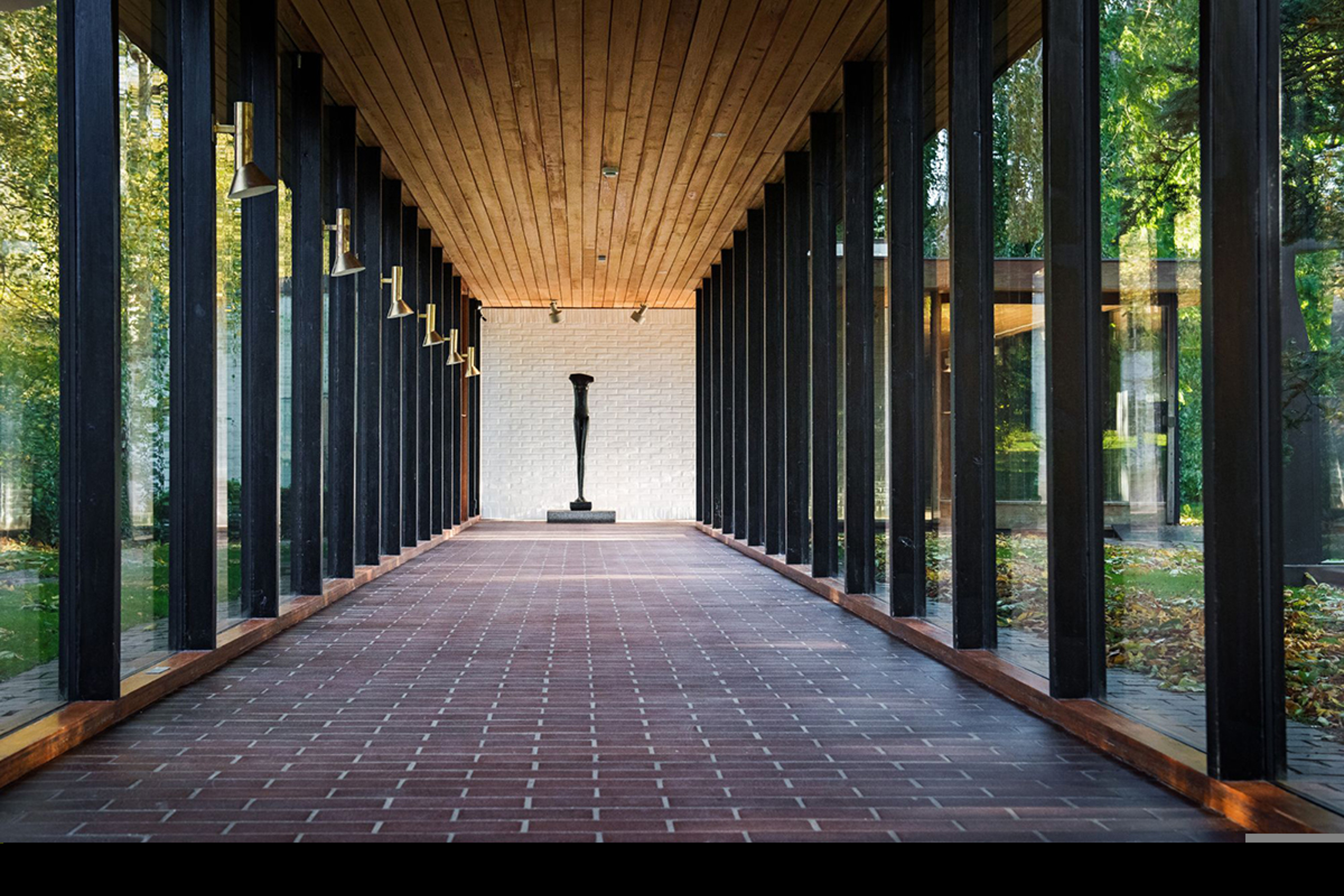 Konstskulptur i slutet av en glasgång med tegelgolv och trätak på Louisiana Museum.
