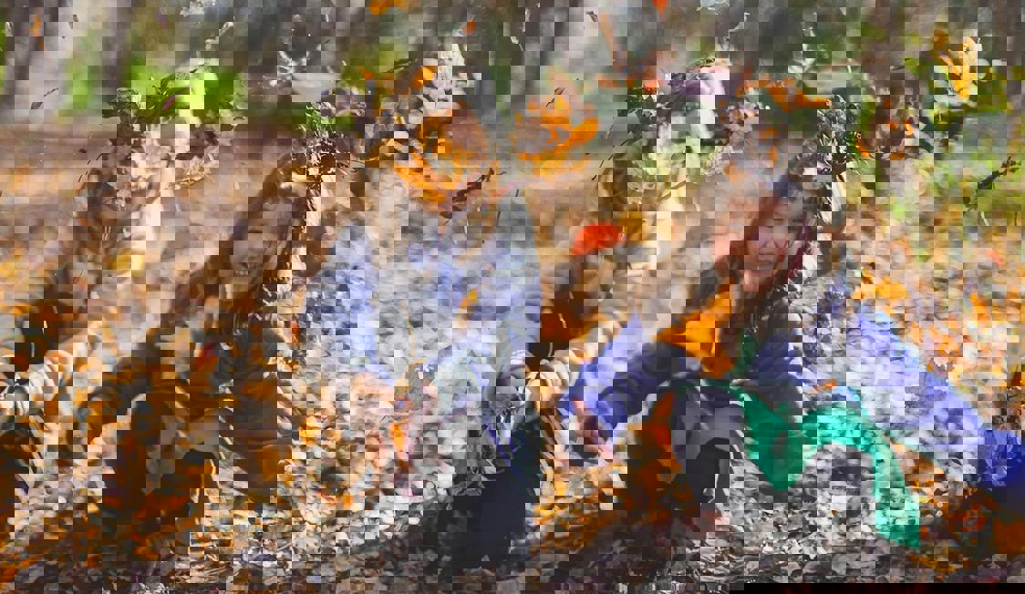 To børn leger i efterårest visne blade i en skovbund.