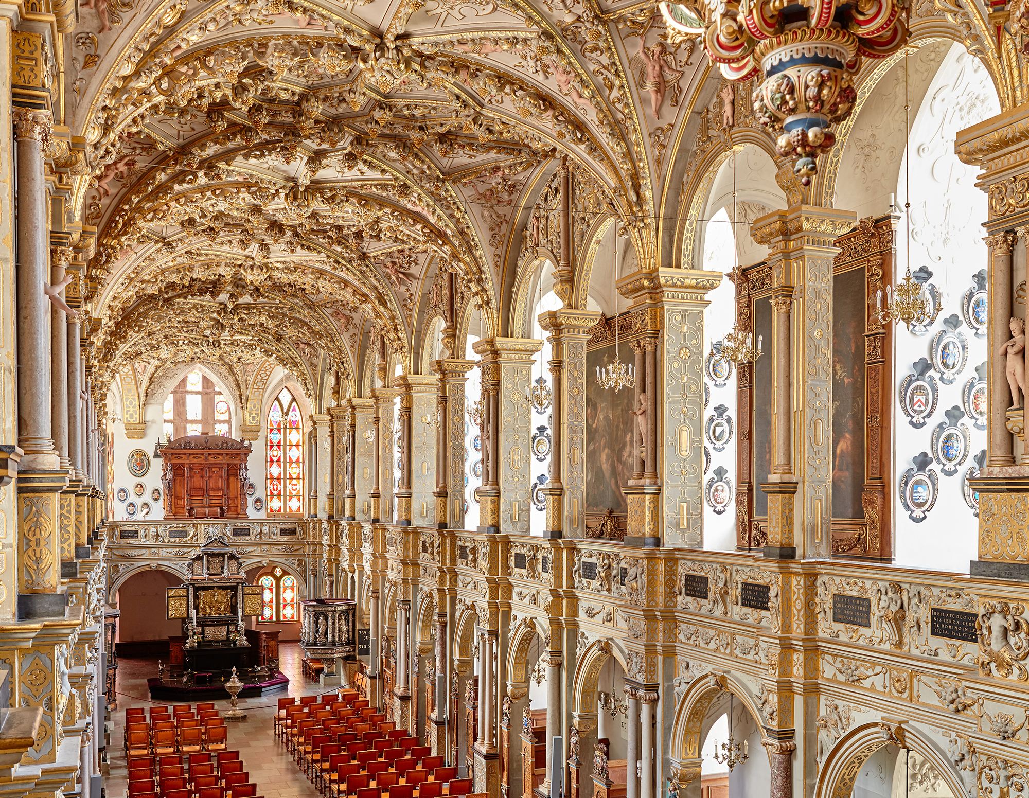 Historisk sal med udsmykkede guldlofter og rækker af røde stole i Weimar i fugleperspektiv.