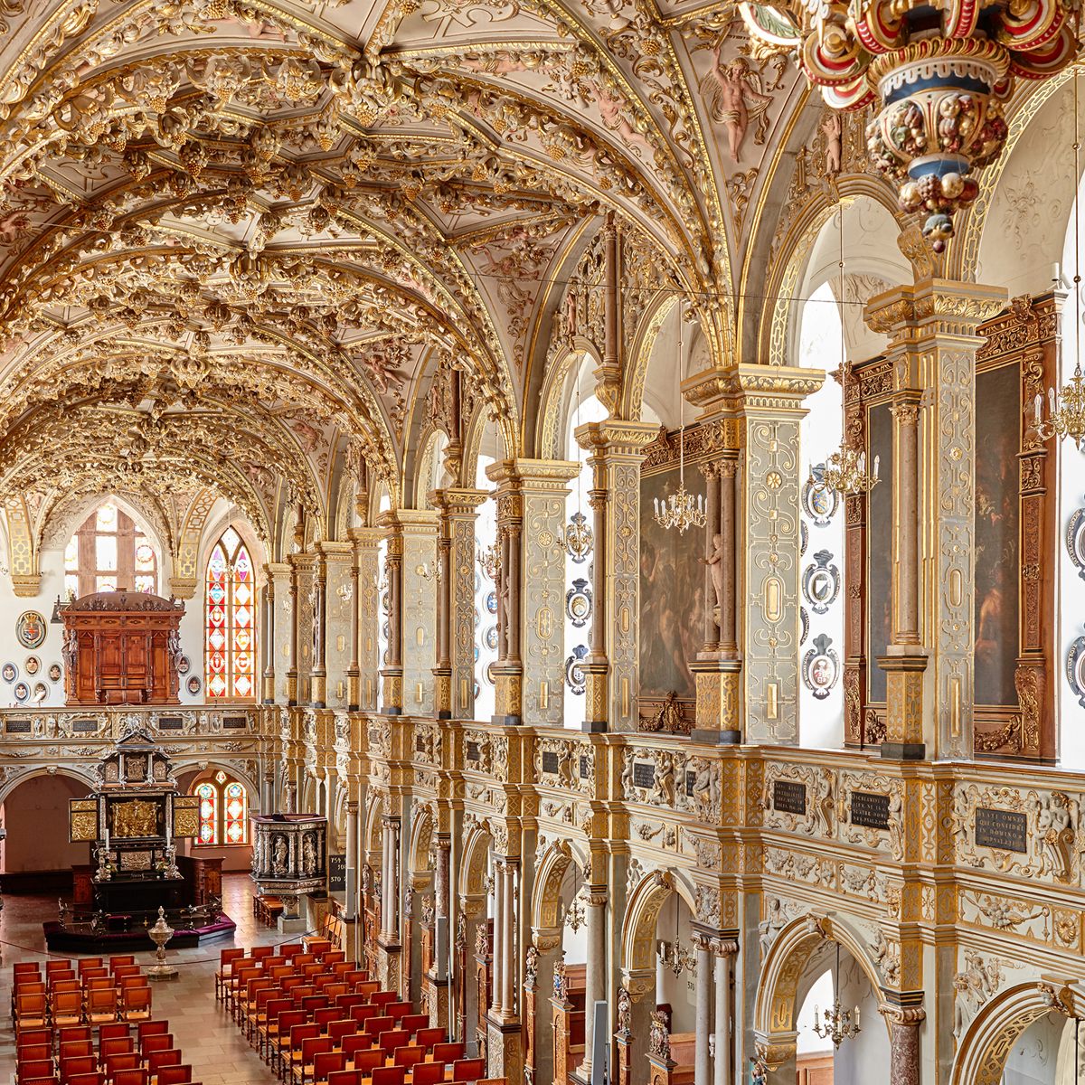 Historisk sal med udsmykkede guldlofter og rækker af røde stole i Weimar i fugleperspektiv.