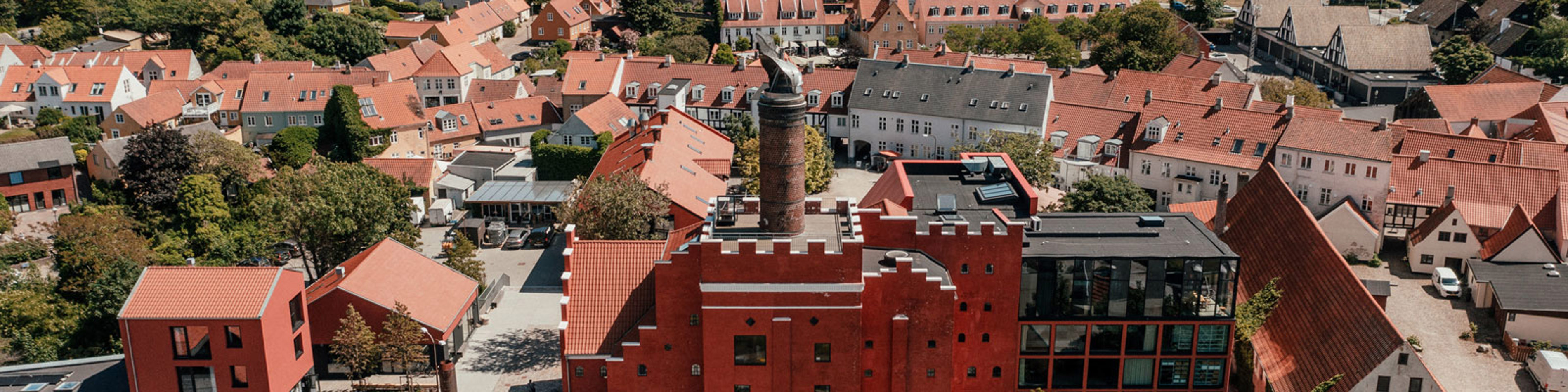 Rødt murstensslot med tårn set fra luften omgivet af charmerende byhuse med røde tage i Svaneke, Bornholm.