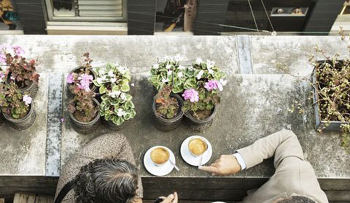 Två personer njuter av kaffe på takterrassen i Köpenhamns Illum med utsikt och blommor i bakgrunden.