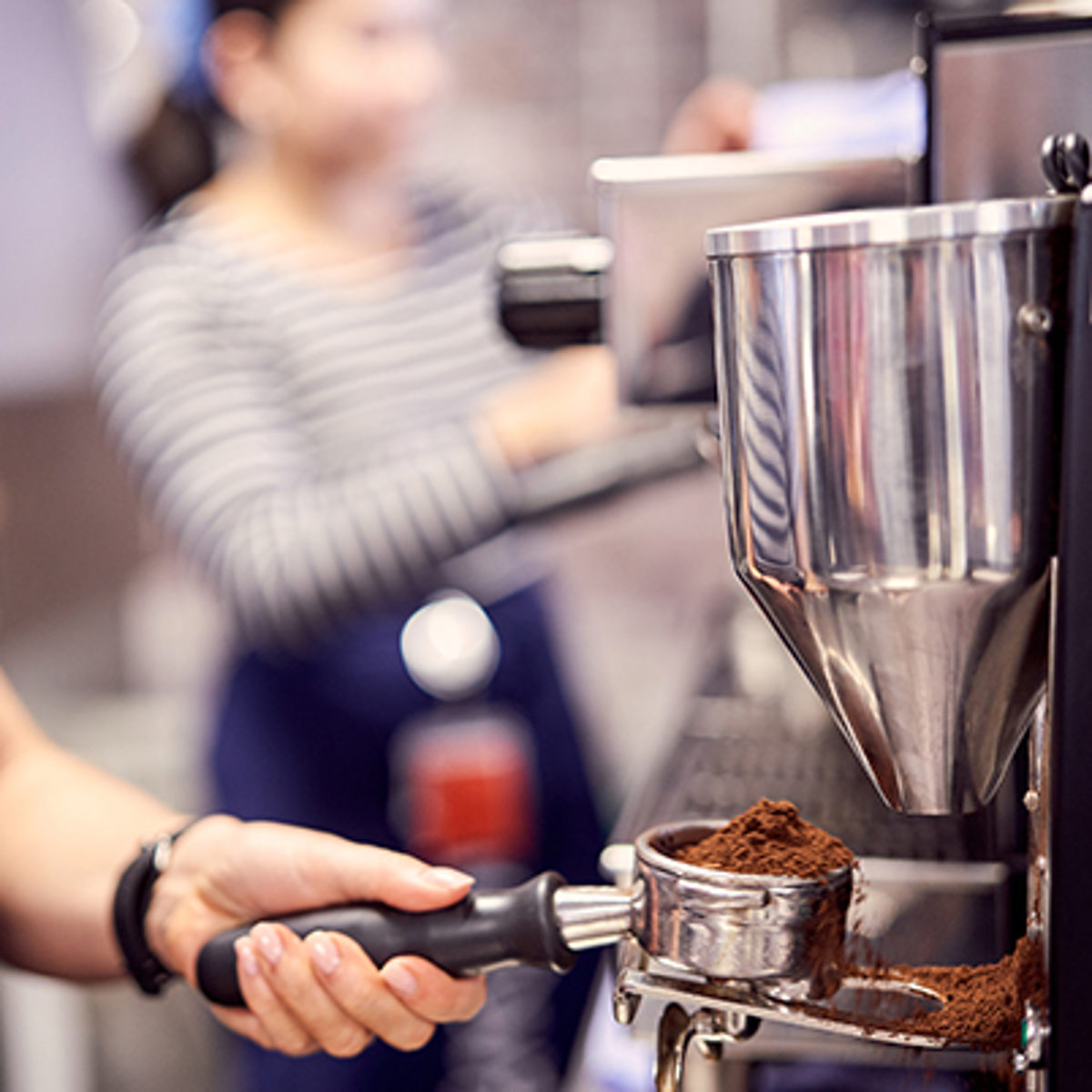 Barista maler kaffebønner med en kommerciel espressomaskine i et travlt kaffehusmiljø.
