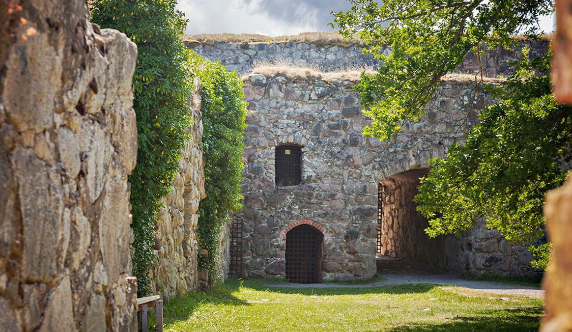 Stenmure i en middelalderlig ruin med buegange omringet af natur på en solrig dag i fugleperspektiv.