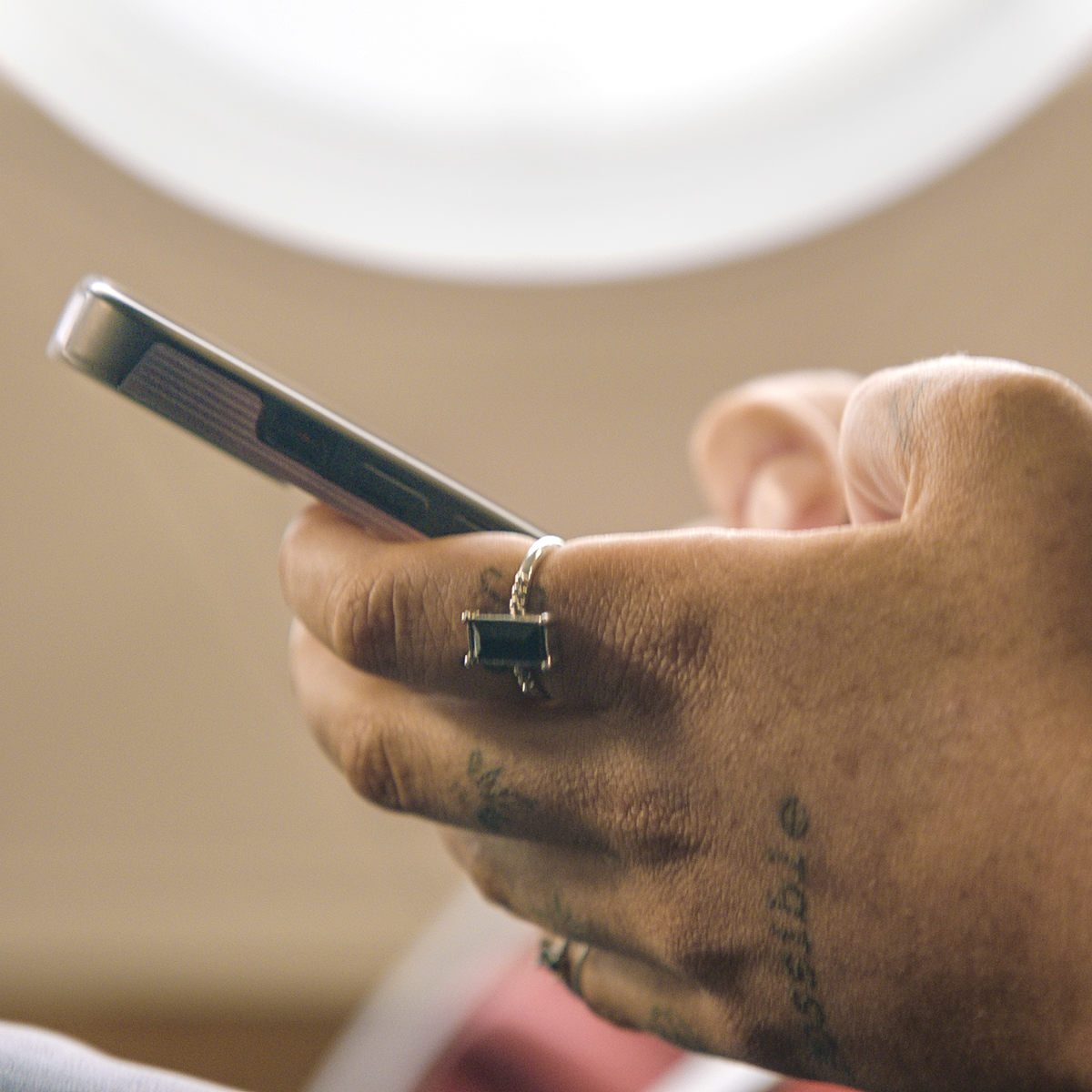 Person med håndtattoo skriver på smartphone ved et vindue.