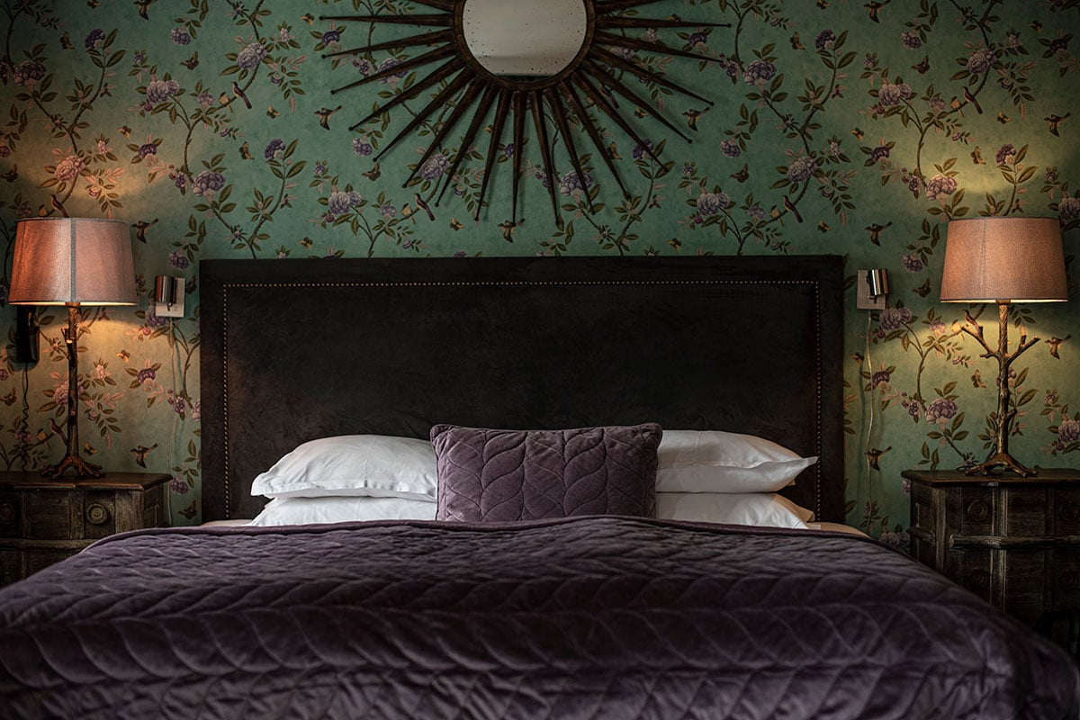 V hotel værelse ses fra fodenden af sengen, der er redt med et fløjlsengetæppe.