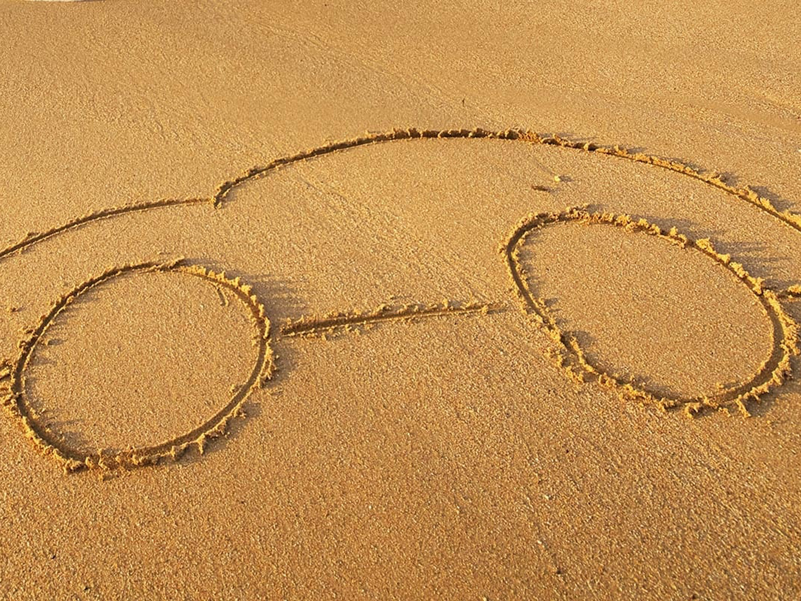 Bilform ritat i sanden på stranden.