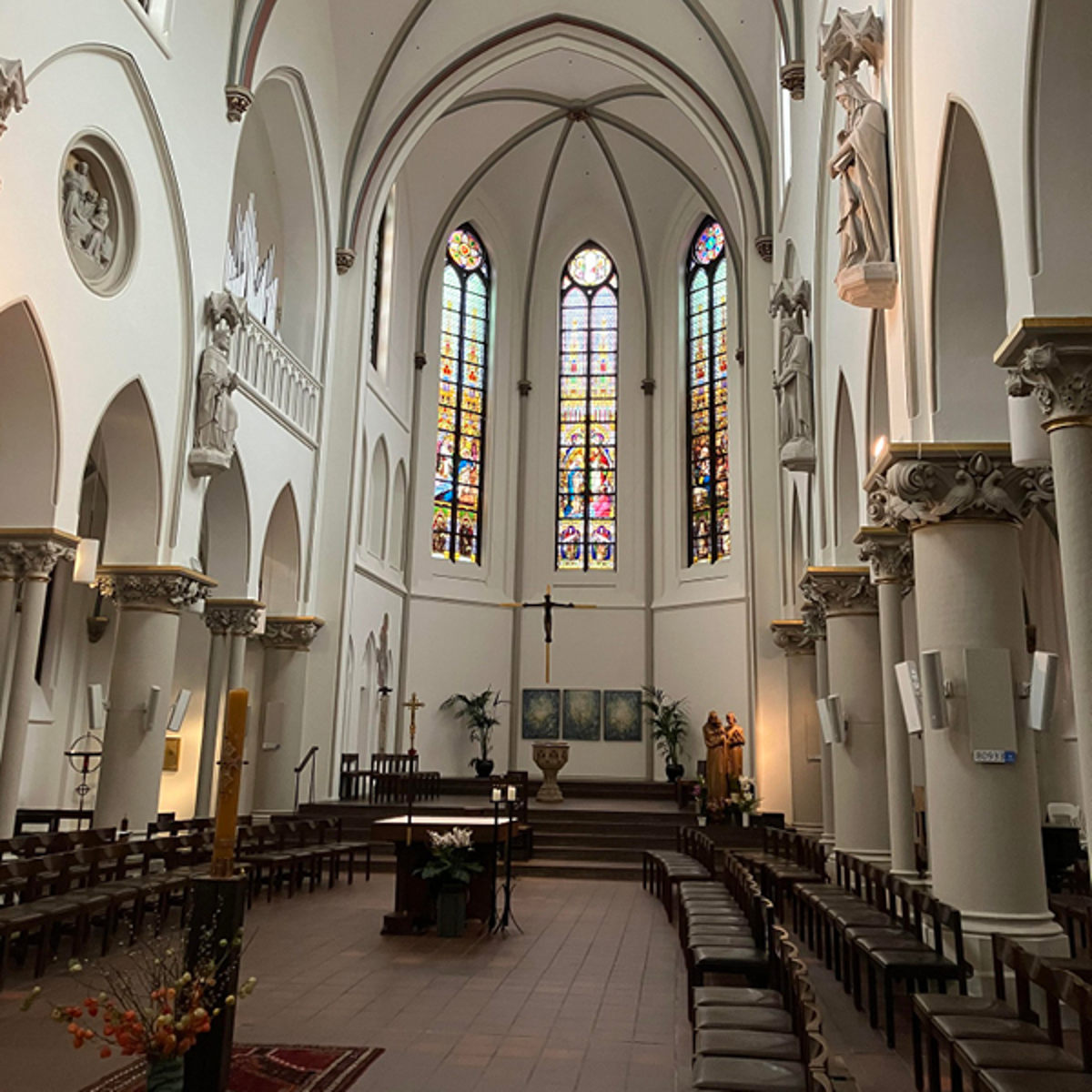 Indre udsigt af en gotisk kirke med buede lofter og farverige glasmosaikvinduer.