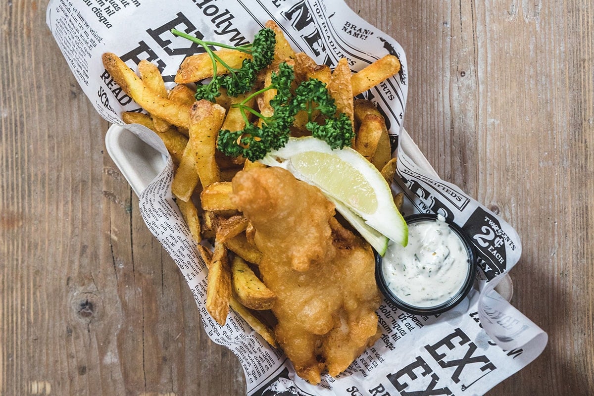 Närbild på fish n chips på ett träbord.