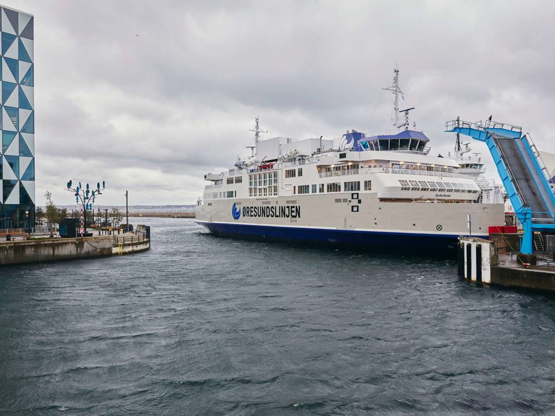 Øresundslinjen færge nærmer sig havnen under overskyet himmel med moderne arkitektur i baggrunden.