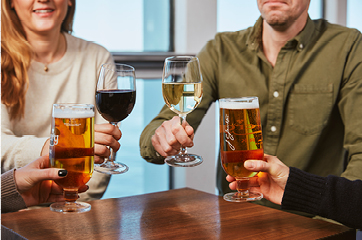 Fyra personer skålar med öl och vin vid ett träbord, närbild av händer och glas.