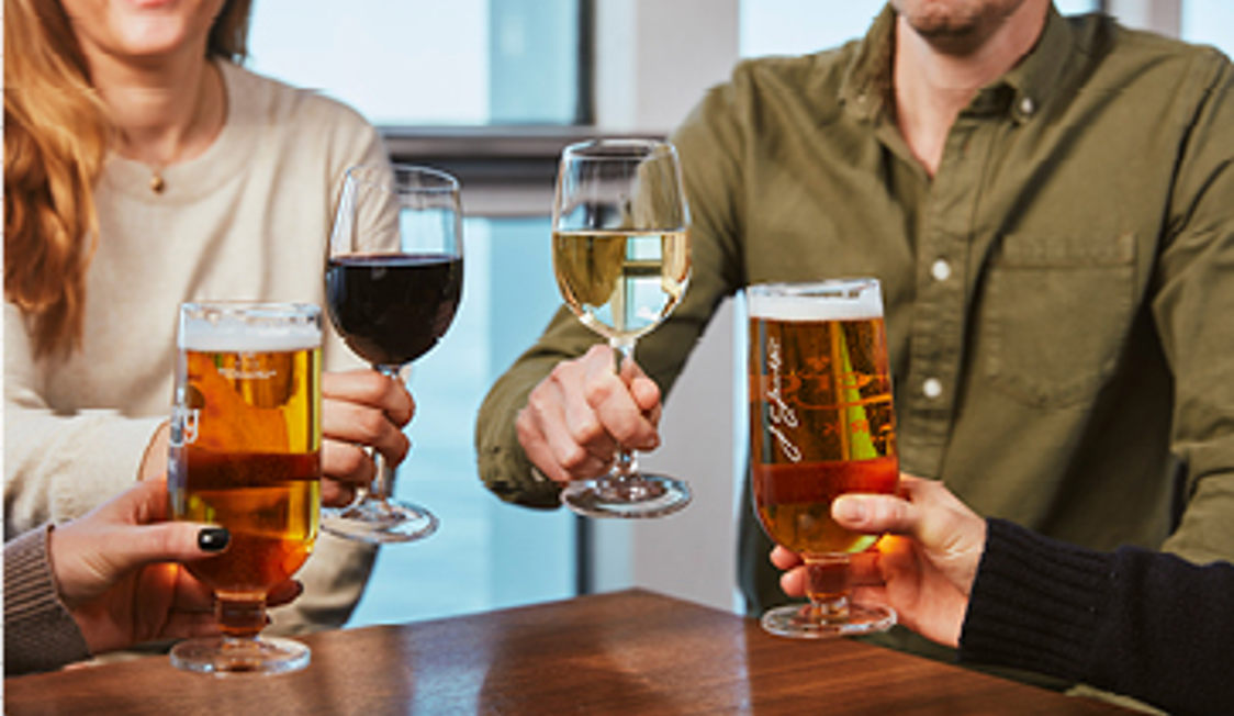 Fire personer skåler med øl og vin ved et bord, set fra nærbillede.