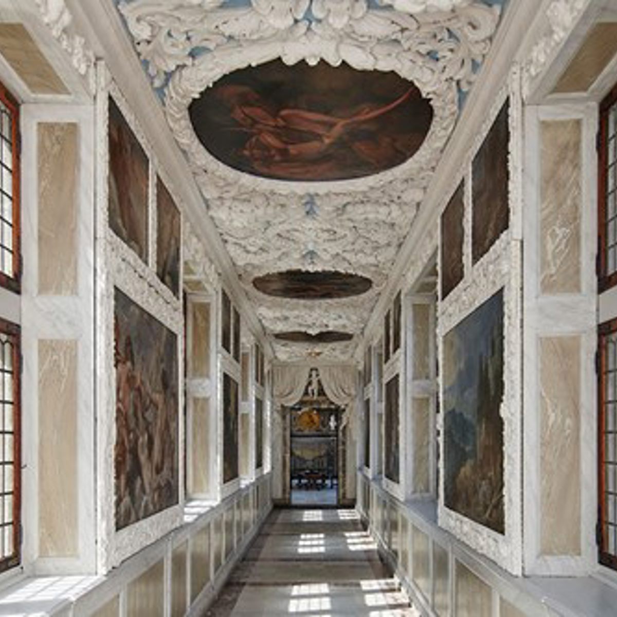 Dekoreret korridor med detaljeret loft og klassiske malerier i et historisk palads.