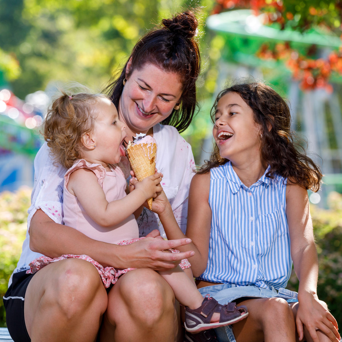 En mamma med två barn som delar en glass i solen under en utomhusutflykt.