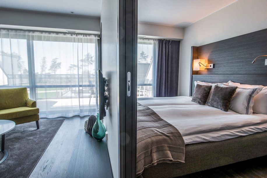 Moderne hotelværelse med dobbeltseng og elegante tekstiler ved siden af skillevæg i skandinavisk design.