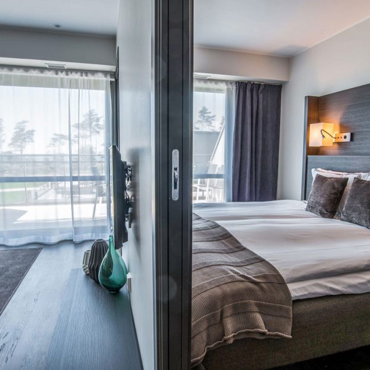 Moderne hotelværelse med dobbeltseng og elegante tekstiler ved siden af skillevæg i skandinavisk design.