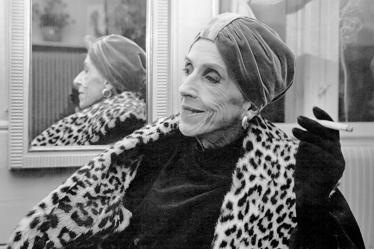 Karen Blixen sidder med et skævt smil i sort/hvid.