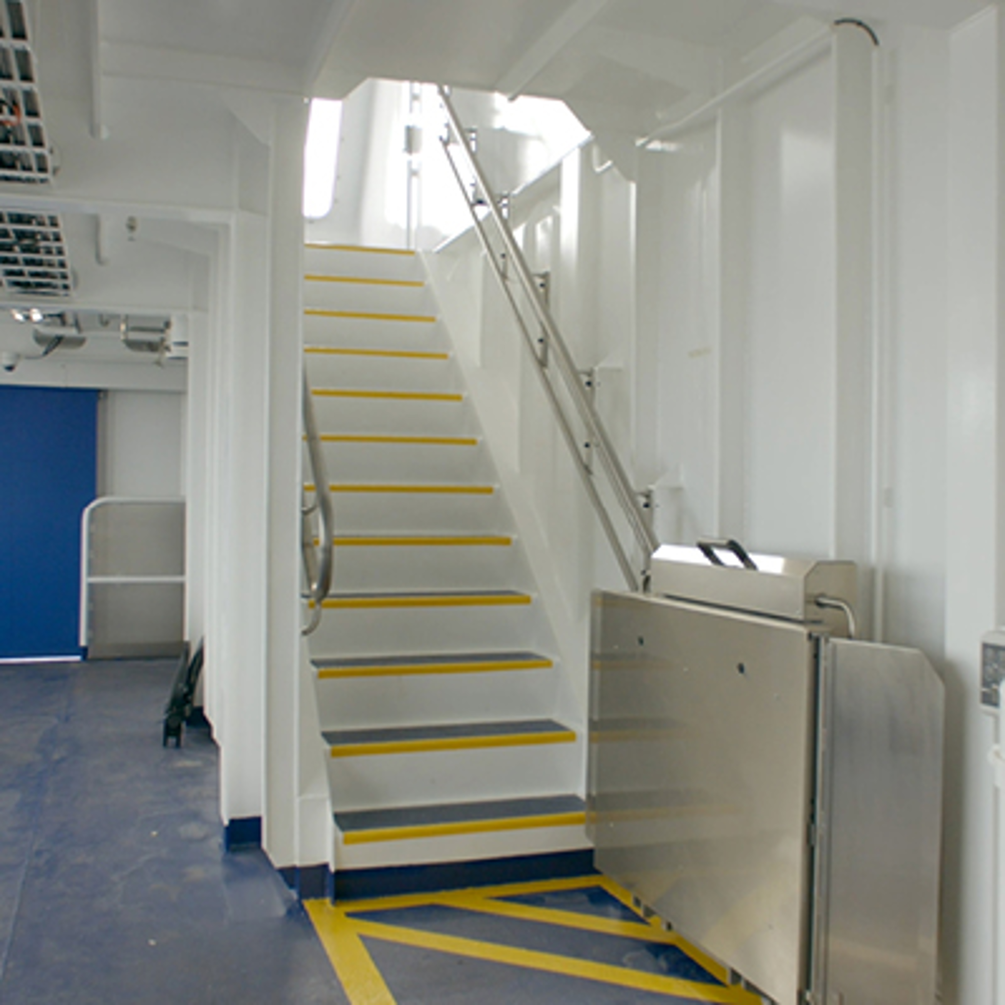 Indendørs trappe på Molslinjen færge med hvidt gelænder og gule trinmarkeringer, set fra siden.