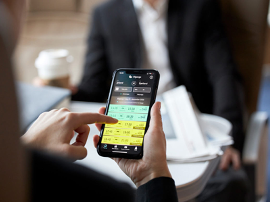 Eine Person benutzt ein Smartphone, um eine Fährverbindung in der Molslinjen Business Lounge zu buchen.