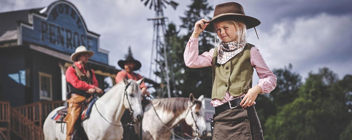 Et barn i cowboy udstyr og to mænd på heste ses i forgrunden af High Chaparral.