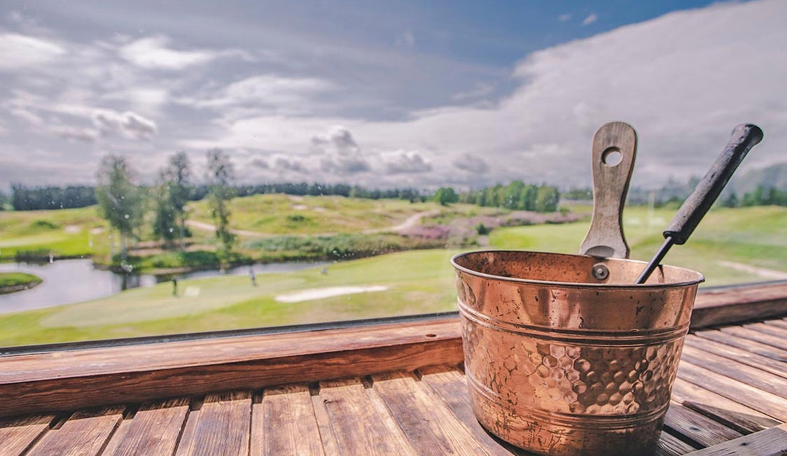 Kobberspand med metaltang står på træbord foran udsigt til golfbane og skov.