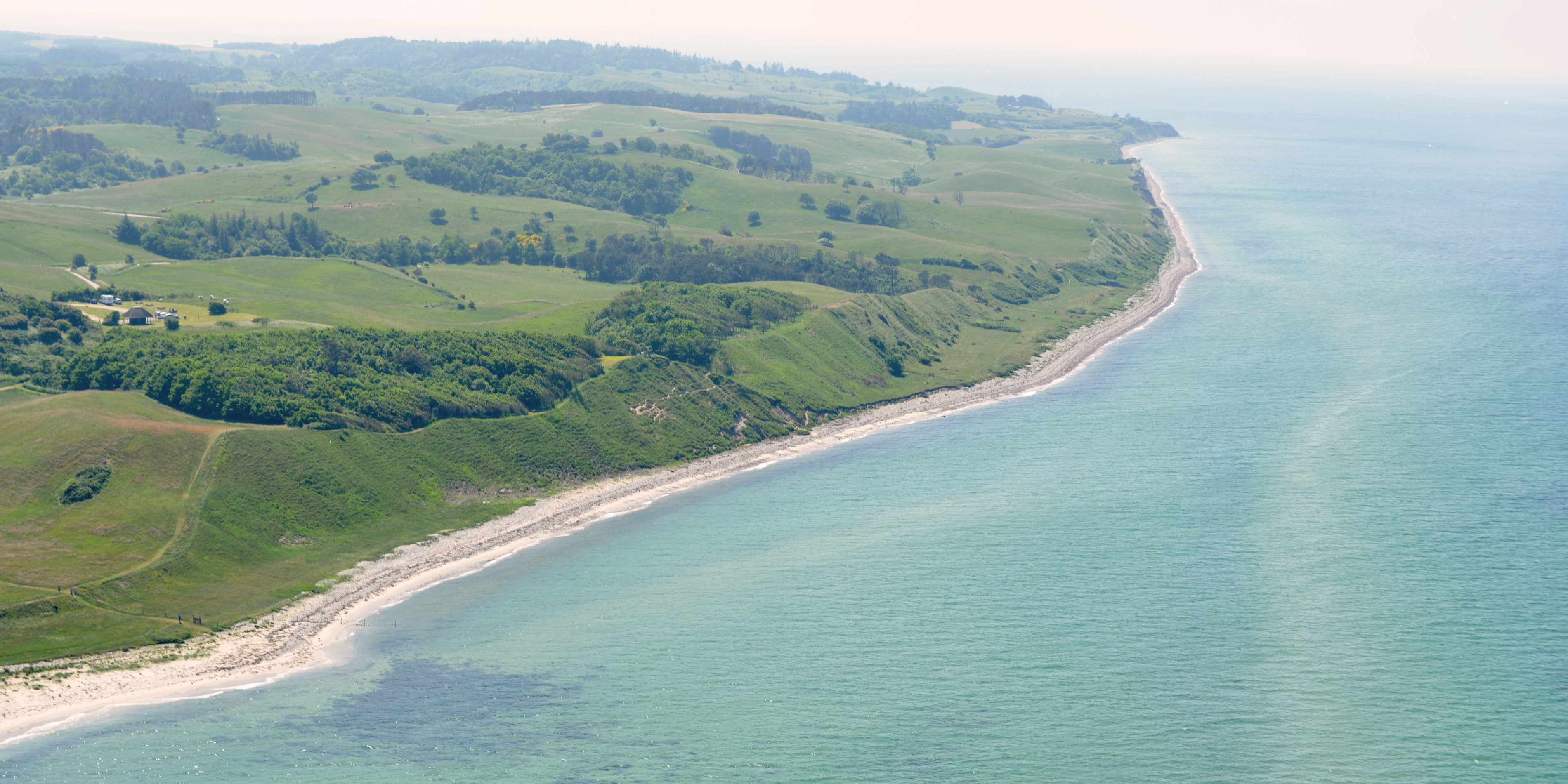 Kystlinje set fra luften viser en grøn bakket landskab og hav ved Mors, Danmark, med dramatisk udsigt og klare farver.