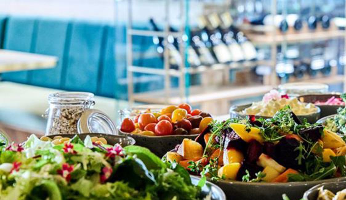 Friske salater med farverige grøntsager og frugt serveret i skåle på en restaurantbuffet i elegant indretning.