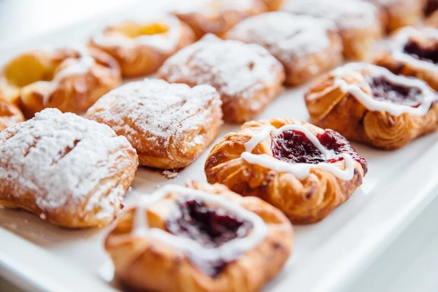 Friske danske wienerbrød med glasur og bærfyld, serveret på en hvid bakke i nærbillede.
