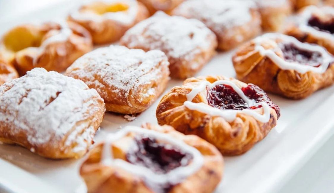 Friska danska wienerbröd med glasyr och bärfyllning, serverade på en vit bricka i närbild.