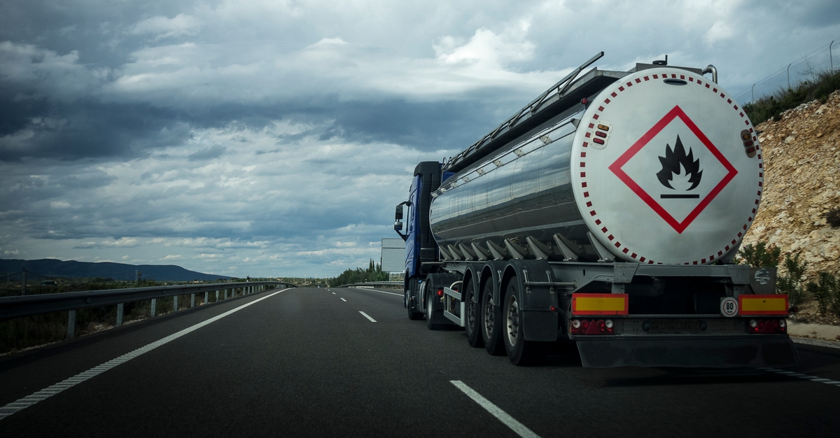 Tanker truck transporting flammable materials on an open highway under a cloudy sky.