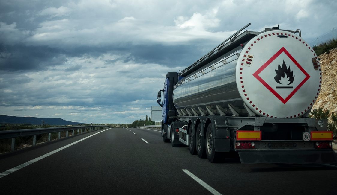Tanker truck transporting flammable materials on an open highway under a cloudy sky.