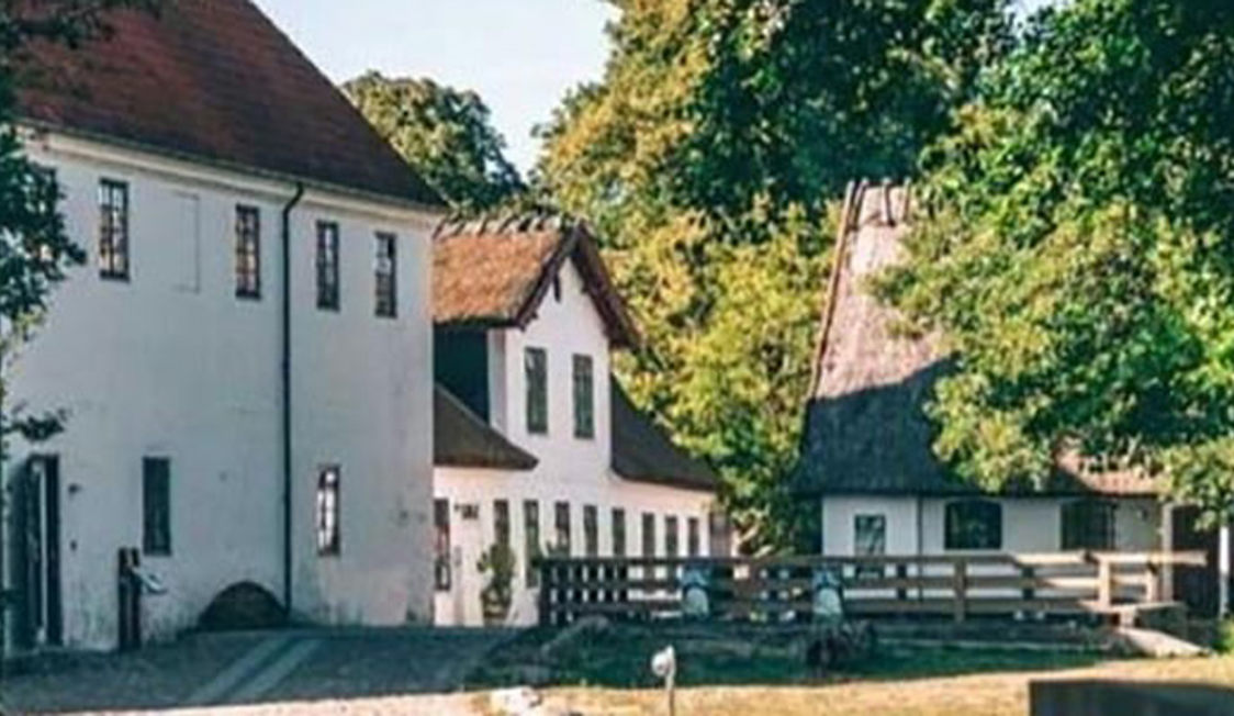 Vit historisk byggnad av Esrum Kloster med traditionellt tak mitt i grönskande omgivning.