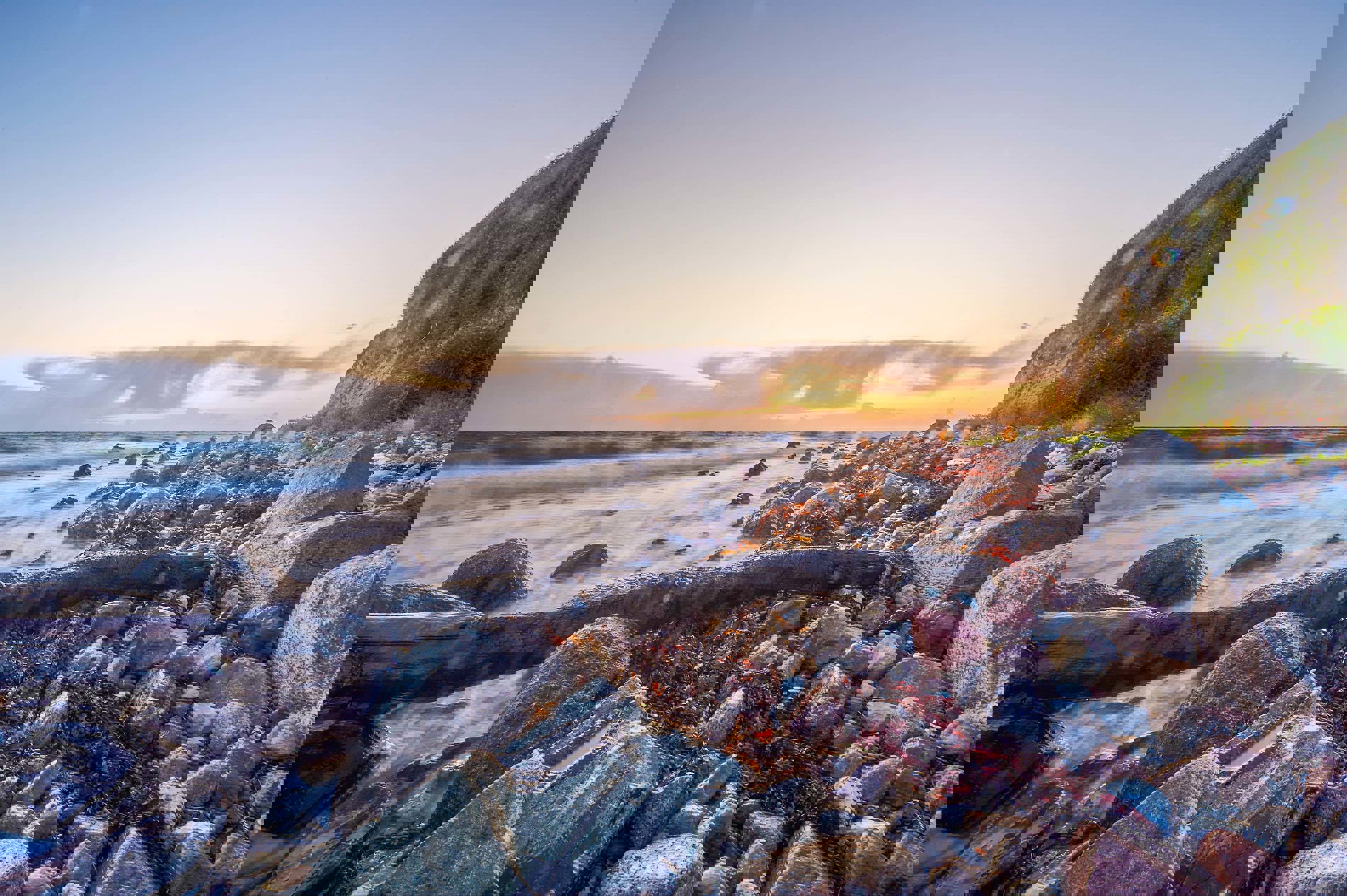 En stenfyldt strand på Samsø ses med solen, der går ned i baggrunden.