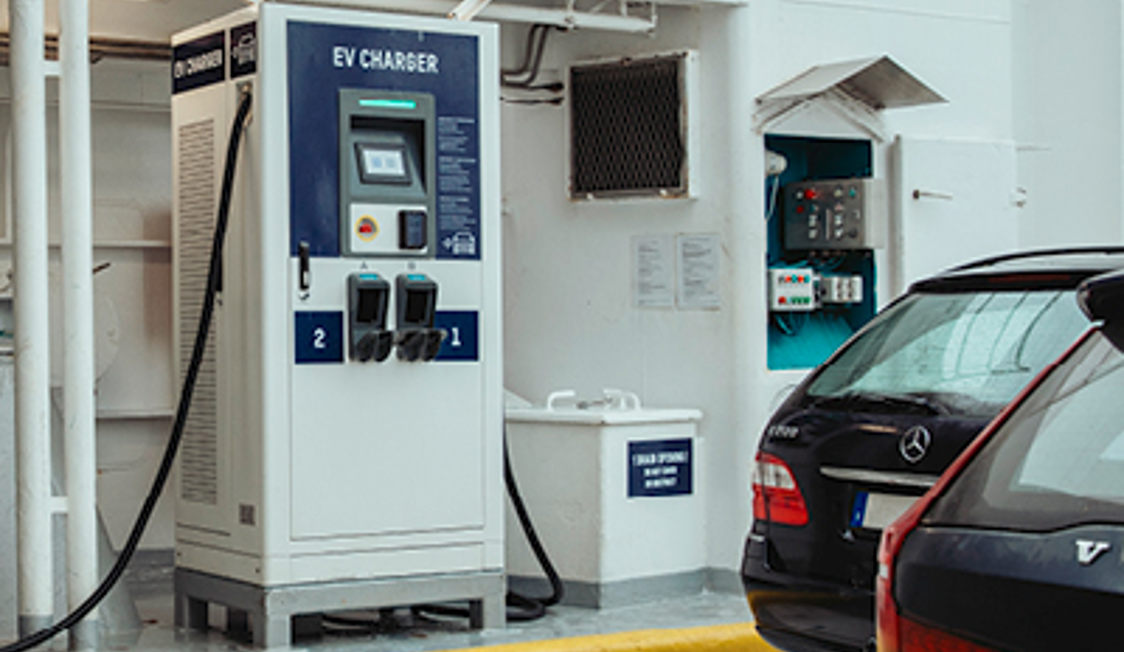 Elbil-ladestation med to udgange står ved siden af sorte biler i parkeringskælder.