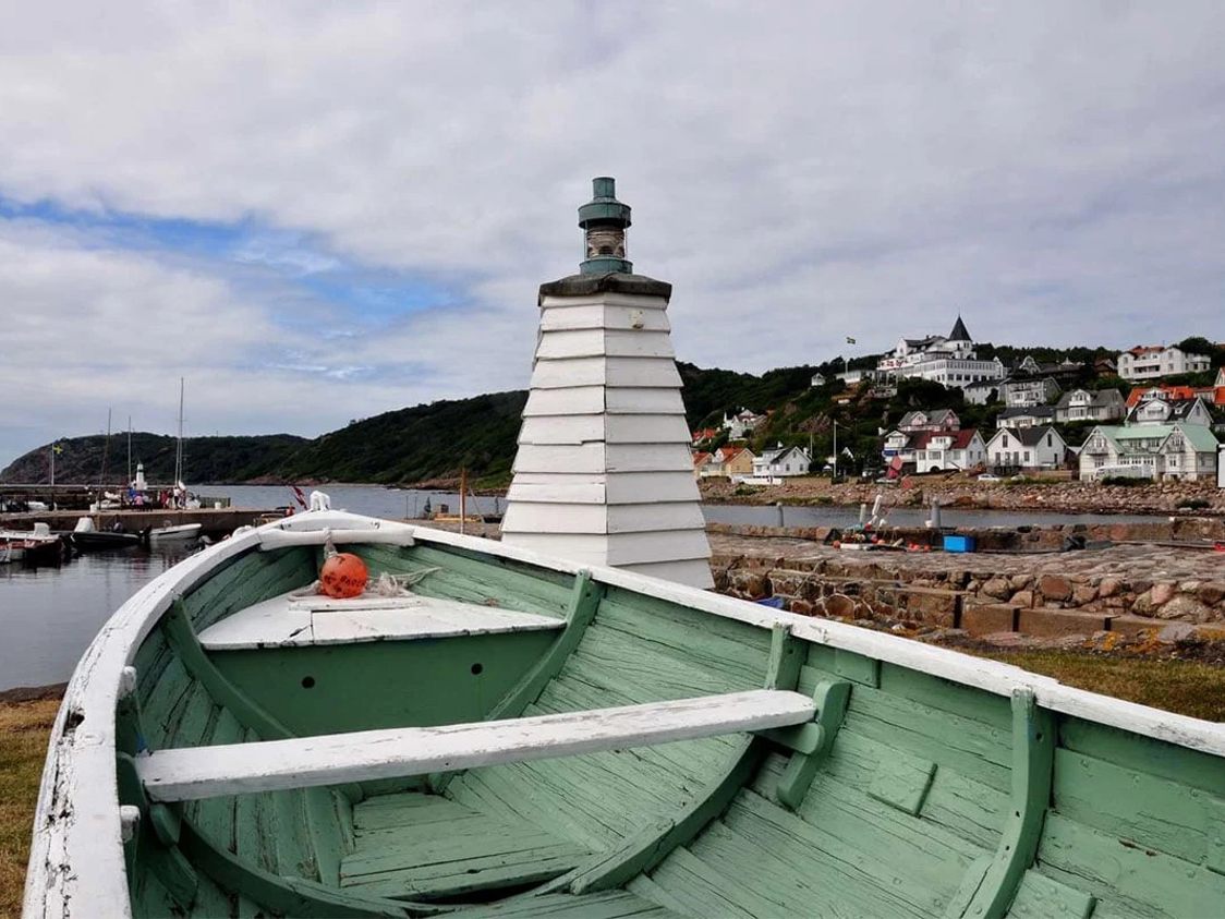 Gammel træbåd med grøn indvendig maling nær Kullens fyr i Mölle med udsigt over havn og malerisk kystby.