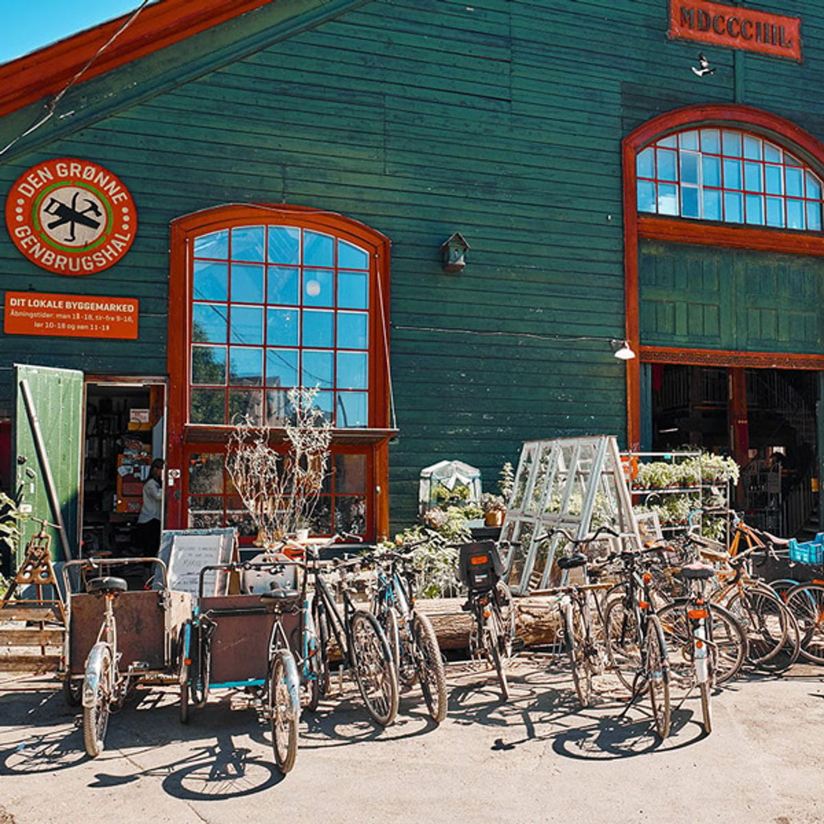 Cyklar framför grönt trähus på Christiania återvinning i Köpenhamn på en solig dag.