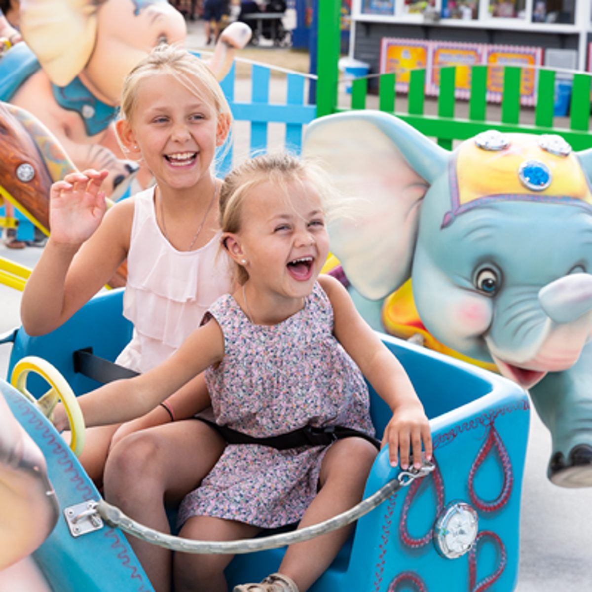 To små piger nyder en tur i en farverig karrusel med elefant, griner og har det sjovt.